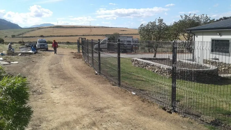 Black Clearview mesh fence and sliding driveway gate at Western Cape farm with rolling wheat fields backdrop