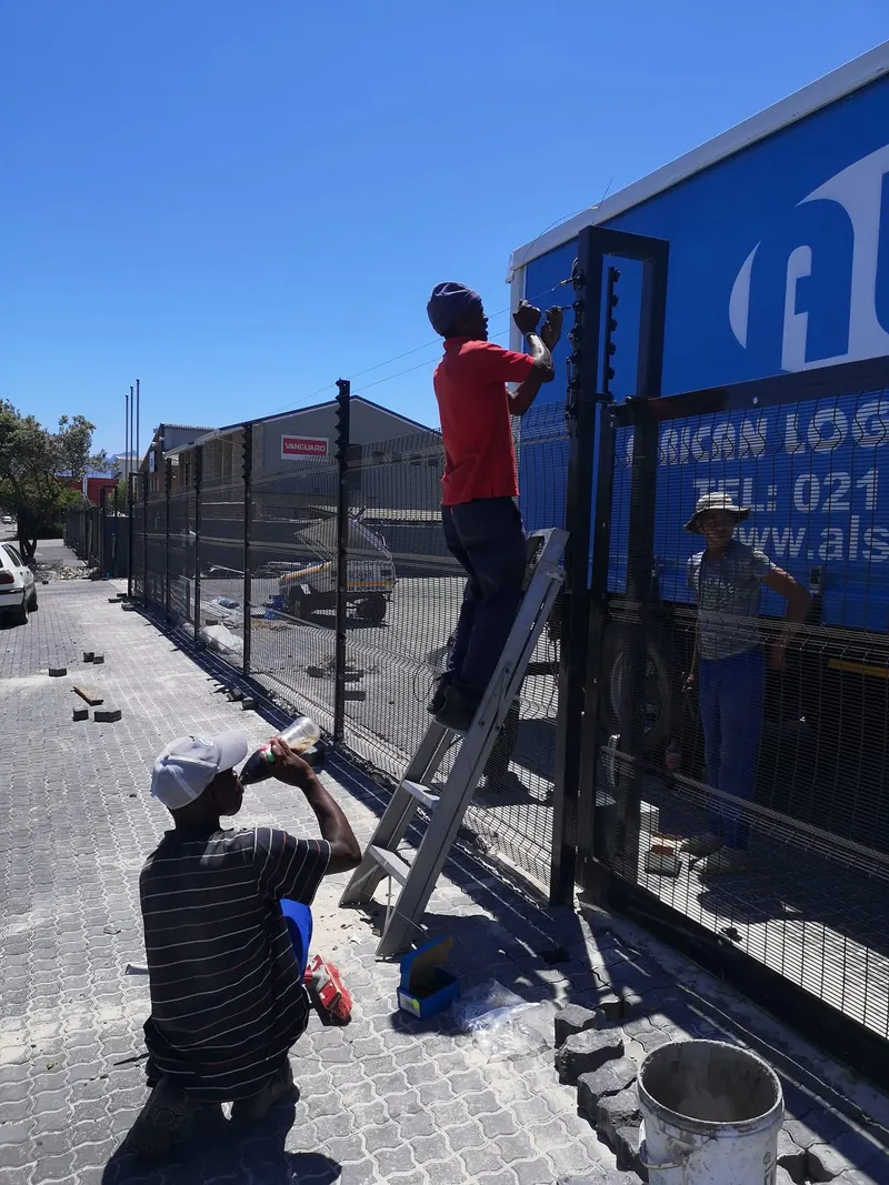 Installer fitting electric fence wires above clearview mesh at commercial depot in Cape Town