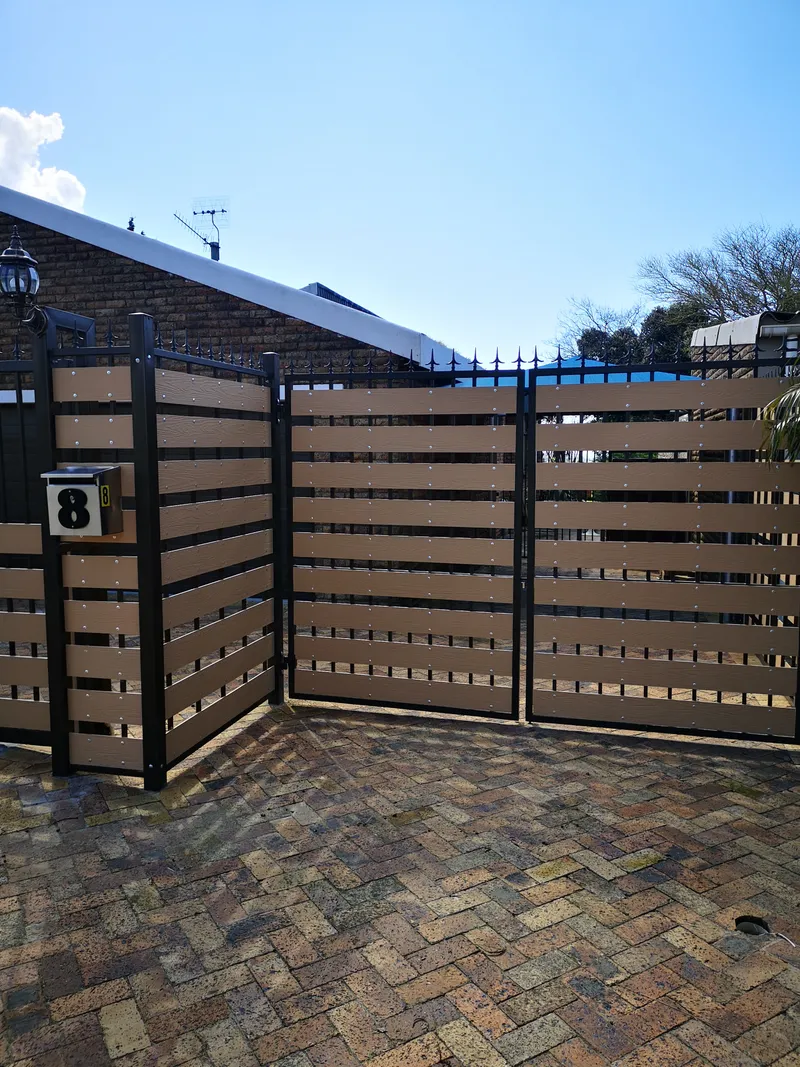 Composite slat driveway gate and matching boundary fence with spike tops on paved driveway in Cape Town