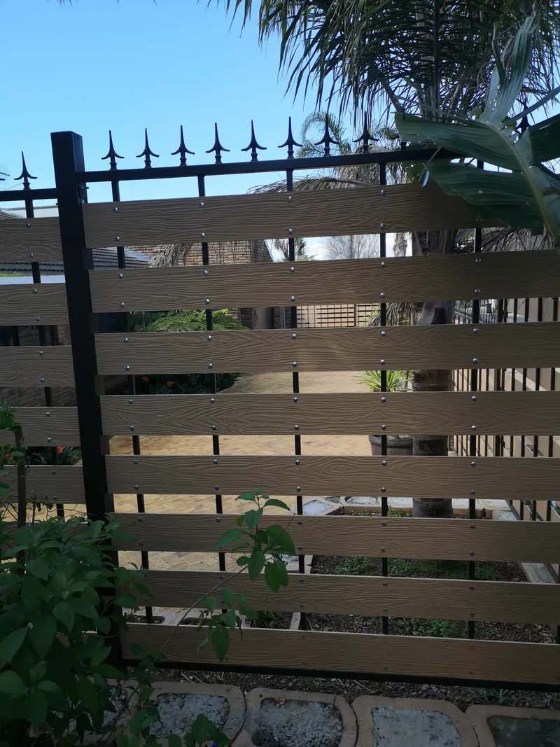 Woodgrain composite slat boundary fence with decorative palisade spike tops at Cape Town residential garden