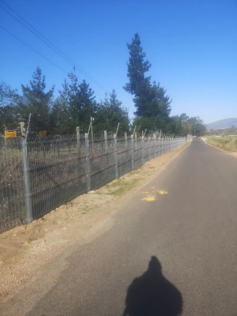 Long galvanised clearview perimeter fence with electric wires along farm road in Western Cape