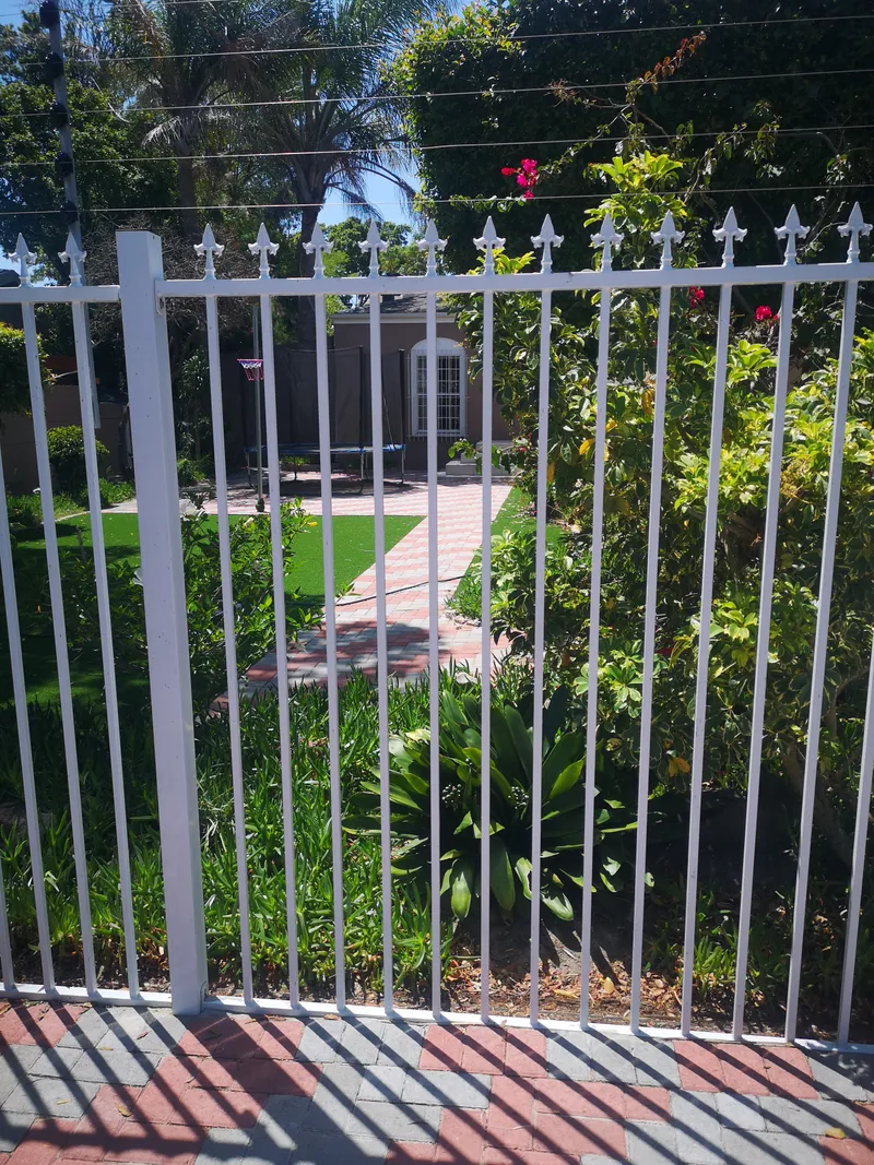 White tubular bar fence with electric top wires fronting residential garden in Cape Town