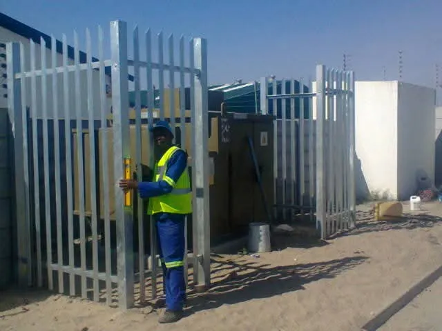 D&H Fencing installer levelling a galvanised steel palisade gate panel with flat pales and three-spike tops at a Cape Town utility site