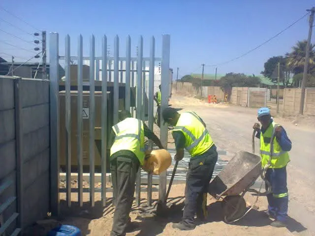 D&H Fencing crew installing galvanised steel palisade fencing at a utility site in Cape Town with concrete being mixed on site