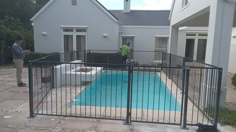 Black powder-coated tubular bar pool safety fence surrounding a residential pool at a Cape Town home with D&H Fencing crew on site