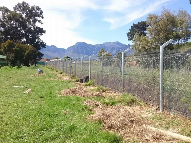 Galvanised high security mesh fence with razor wire topping, mountains in background, Western Cape