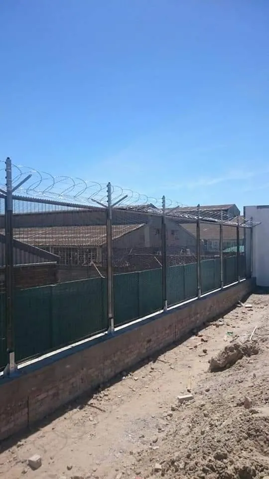 Industrial perimeter mesh fence with brick footing and razor wire coils in the Western Cape