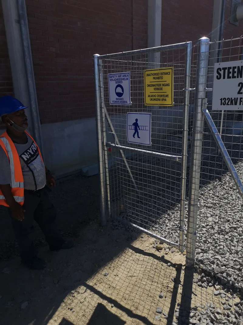 D&H Fencing crew member in hi-vis beside welded mesh pedestrian gate at Cape Town electrical substation