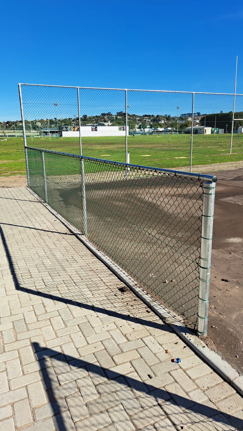 Diamond mesh chain-link fence corner beside sports field with floodlight posts in Cape Town