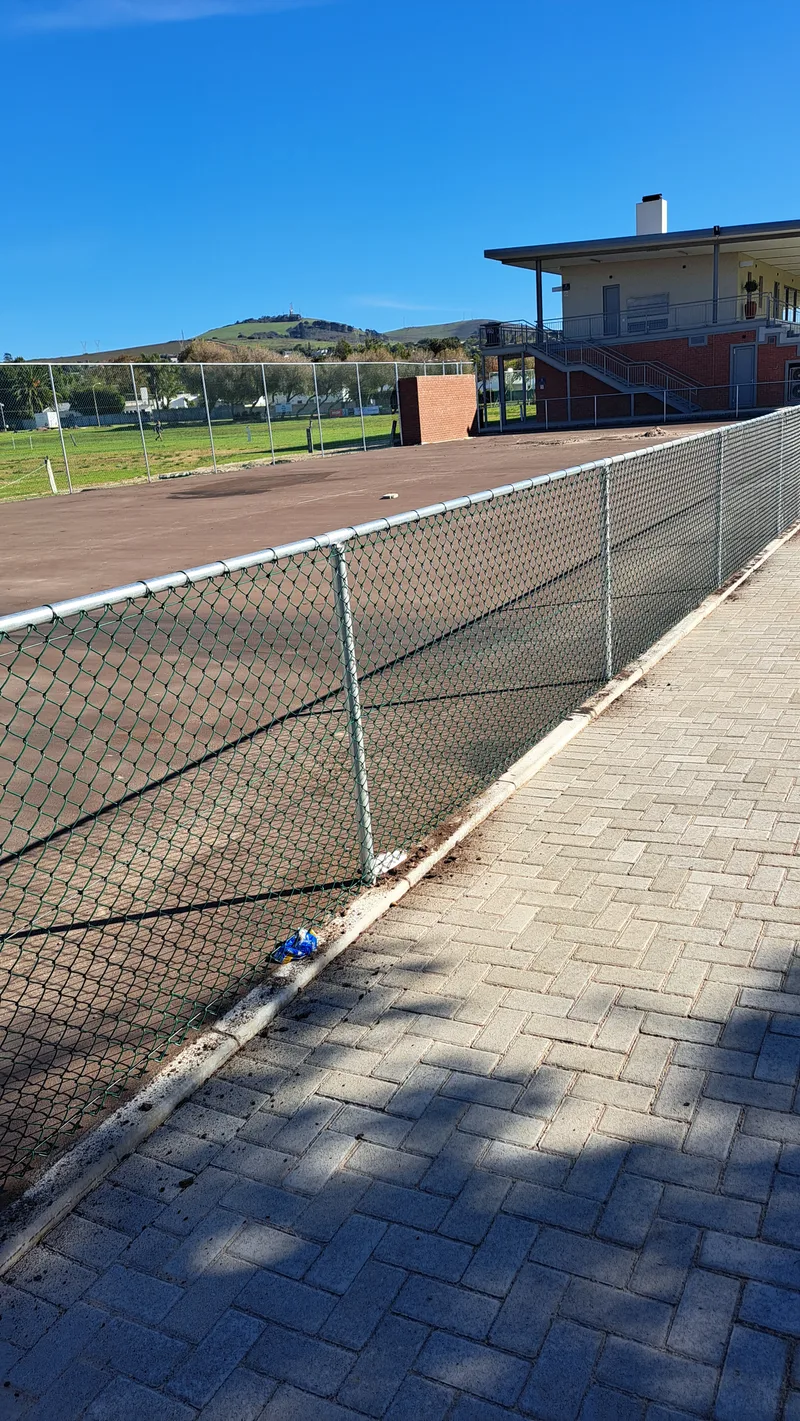 Diamond mesh chain-link boundary fence beside paved walkway at Cape Town school sports facility