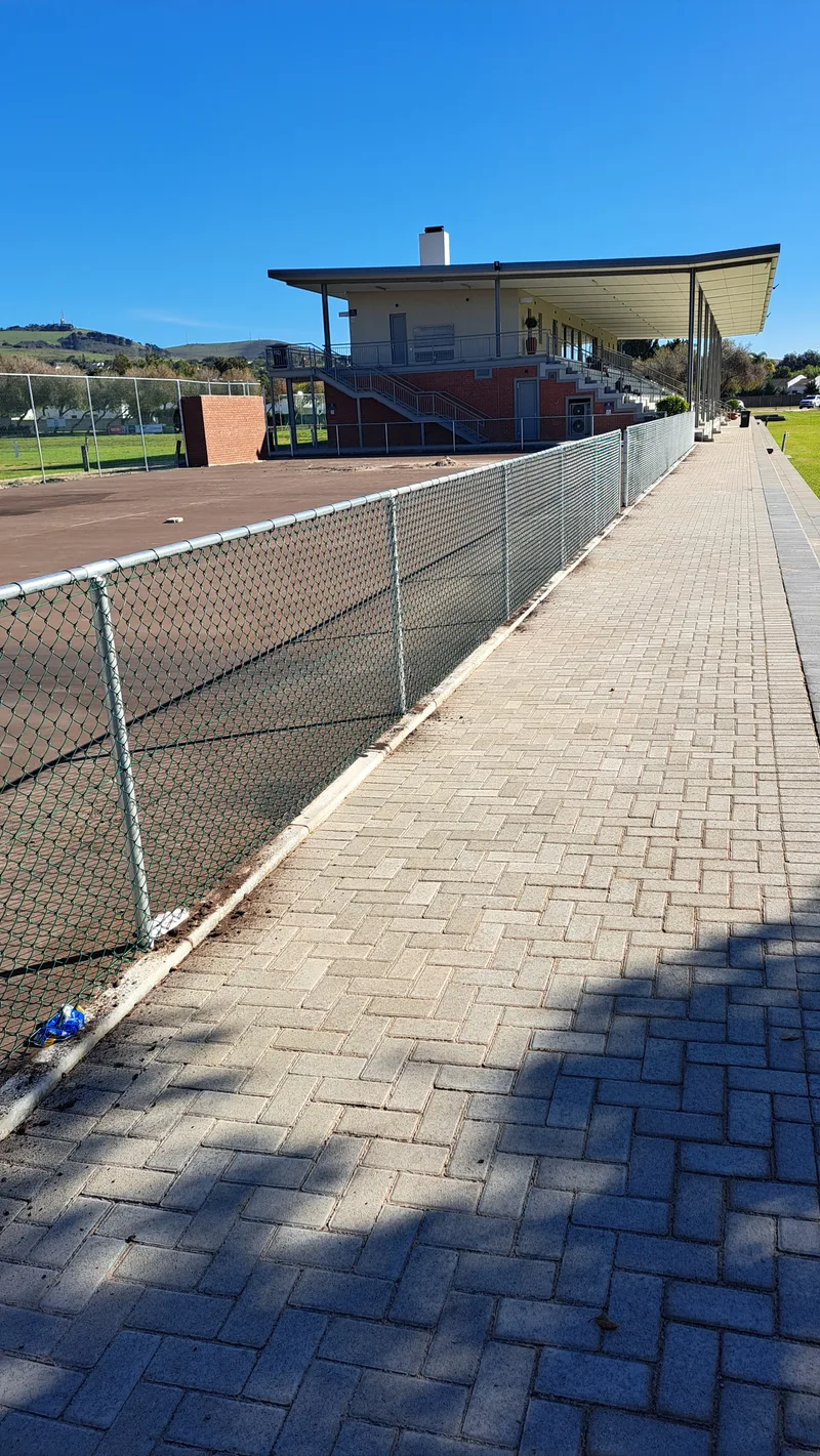Diamond mesh chain-link fence along brick paving and sports building in Cape Town